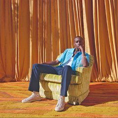 Buddy  Buddy seated behind gold curtains wearing off white high top chucks.