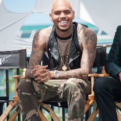 Chris Brown  Chris Brown wearing black high top chucks while sitting in a director’s chair.